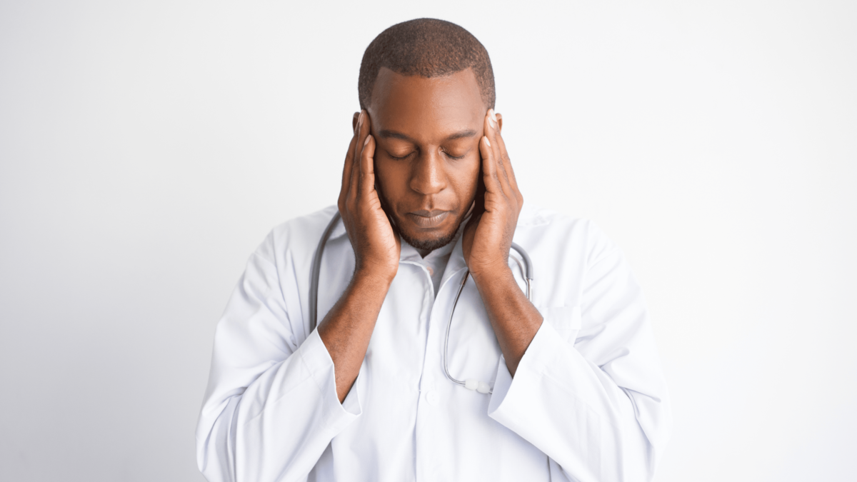 Blog content photo for Physician Physician Wellness in America, depicting a physician holding his head possibly suffering from a headache due to the stress of the Covid-19 pandemic.