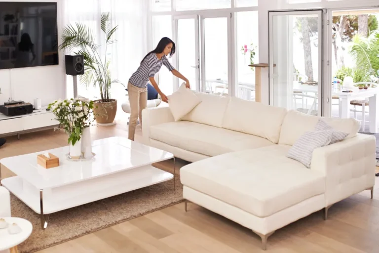 Woman placing pillow on clean white couch in modern spacious living room