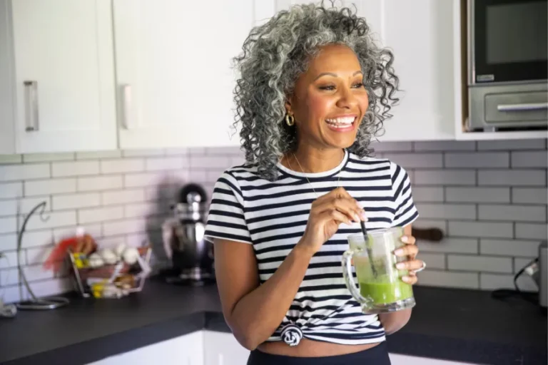 Woman standing in kitchen smiling with vegetable smoothie